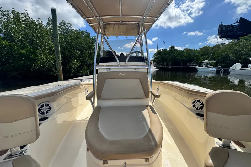 Slide: The Image of 2022 Scout 215 XSF boat interior with seating and canopy, docked near lush greenery. - 18