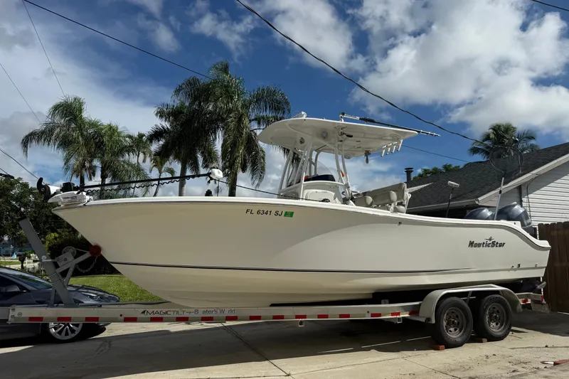The Image of 2015 NauticStar 2500XS Offshore boat on trailer, parked in driveway with palm trees. - 0