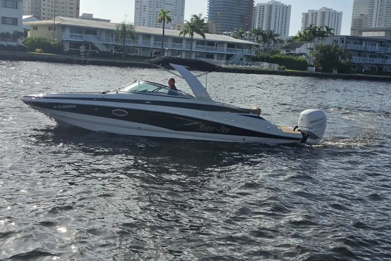 Slide: The Image of 2022 Crownline Eclipse E285 XS boat cruising on a sunny waterfront with cityscape backdrop. - 21