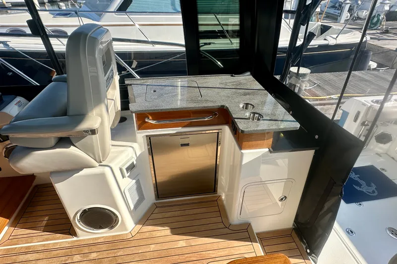 Slide: The Image of 2025 Boston Whaler 365 Conquest interior with helm seat, kitchenette, and wood flooring. - 10