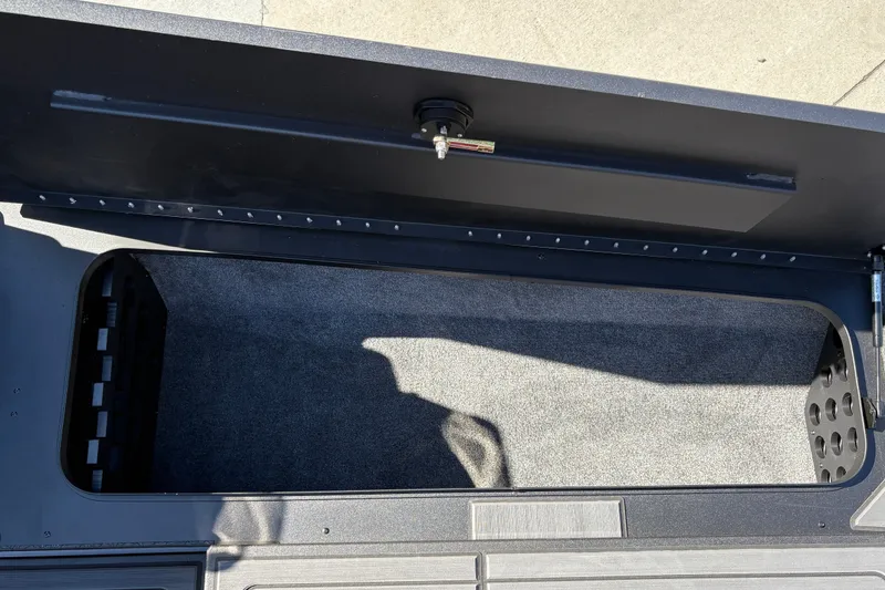 Slide: The Image of Open storage compartment in 2027 Tracker Savage 215 boat, featuring carpeted interior and secure latch. - 34