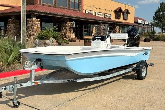 Slide: The Image of 2027 Mako Pro Skiff 17 CC boat on trailer, parked outside a rustic building. - 1