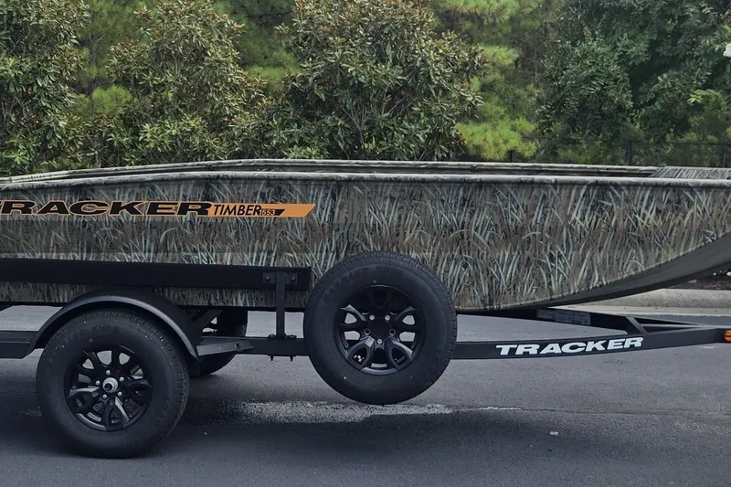 The Image of 2027 Tracker Grizzly 1553 Timber boat on trailer, camo design, parked outdoors. - 0