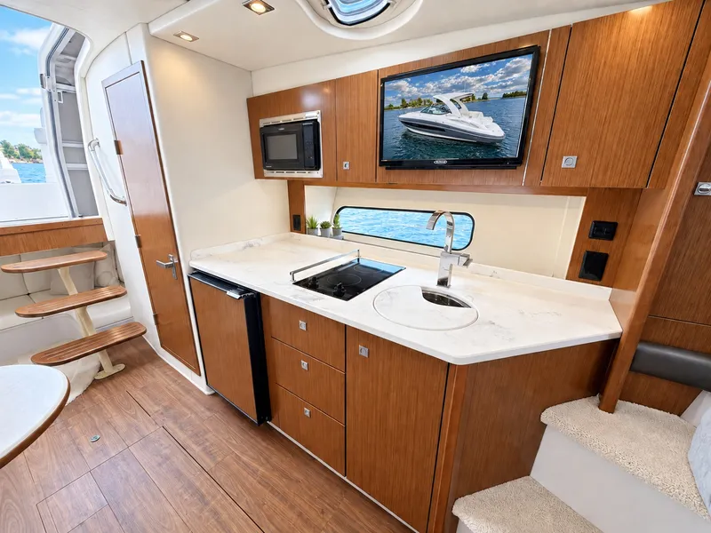 Slide: The Image of The interior of a 2020 Cruisers Yachts 35 Express features a modern kitchen with wood cabinets, sink, and microwave. - 43
