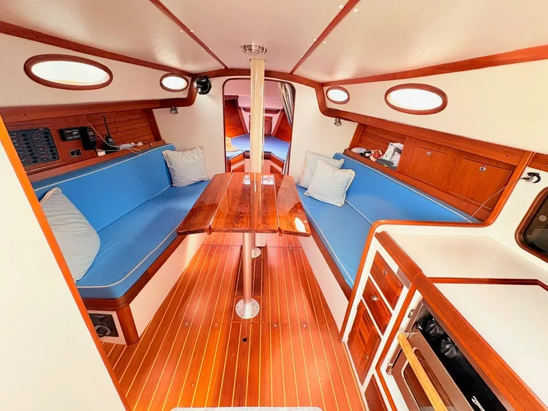 Slide: The Image of The interior of a 2009 Alerion Express 38 features a cozy seating area with blue cushions and a wooden table. - 7