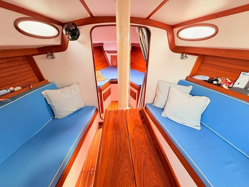 Slide: The Image of The cabin of a 2009 Alerion Express 38 with blue cushions and a wooden table. - 10