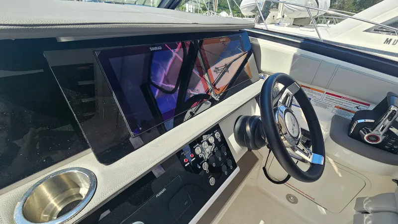 Slide: The Image of The cockpit of the 2024 Sea Ray Sundancer 320 Outboard features a modern dashboard with two large screens and a sleek steering wheel. - 17