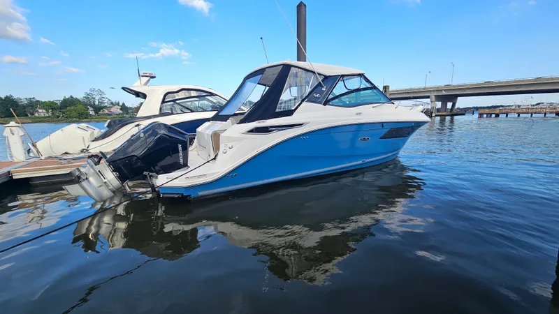 Slide: The Image of A 2024 Sea Ray Sundancer 320 Outboard is docked in the water. The hull is blue. - 1