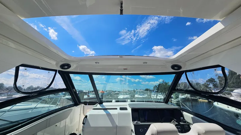 Slide: The Image of The cockpit of the Sea Ray Sundancer 320 Outboard offers a stunning view of the blue sky and marina. - 14