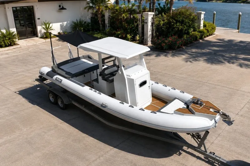 Slide: The Image of 2027 Tide Craft 26 Capri boat on trailer, parked near waterfront property. - 21