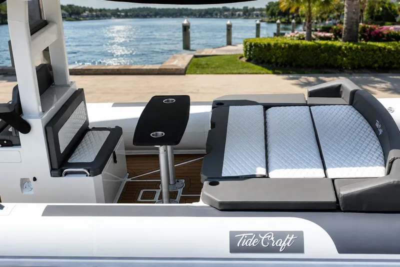 Slide: The Image of 2027 Tide Craft 26 Capri boat interior with seating and table, docked by a scenic waterfront. - 18