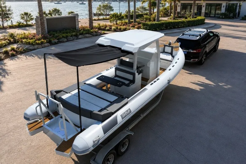Slide: The Image of 2027 Tide Craft 26 Capri boat on trailer, parked near waterfront with SUV. - 20
