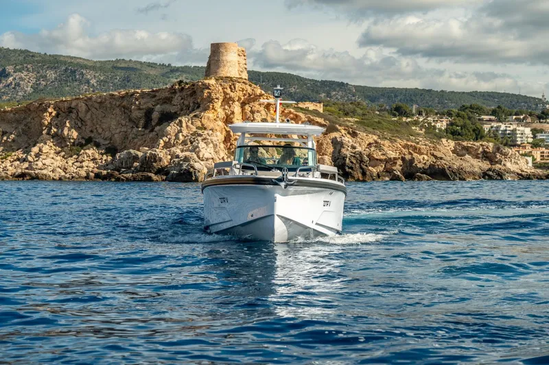 Slide: The Image of 2027 Axopar 29 Sun-Top boat cruising near rocky coastline under cloudy sky. - 1