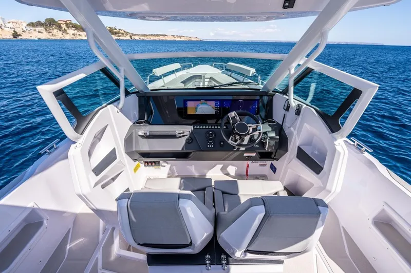 Slide: The Image of 2027 Axopar 29 Sun-Top boat interior with modern dashboard and steering, overlooking blue sea. - 10