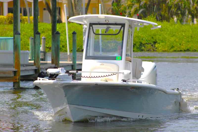 The Image of 2022 Sea Hunt BX25FS boat navigating a calm waterway near docks and greenery. - 0