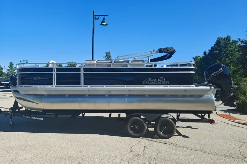 The Image of 2027 Sun Tracker Fishin' Barge 20 DLX pontoon boat on trailer, parked outdoors. - 1