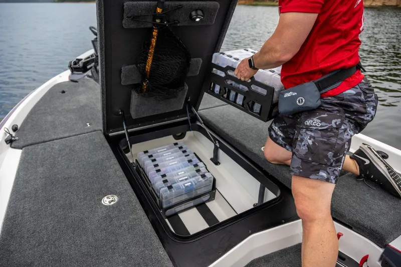 Slide: The Image of Manufacturer Provided Image: 2024 Skeeter FXR21 Apex boat with open storage compartment, person organizing tackle boxes. - 16