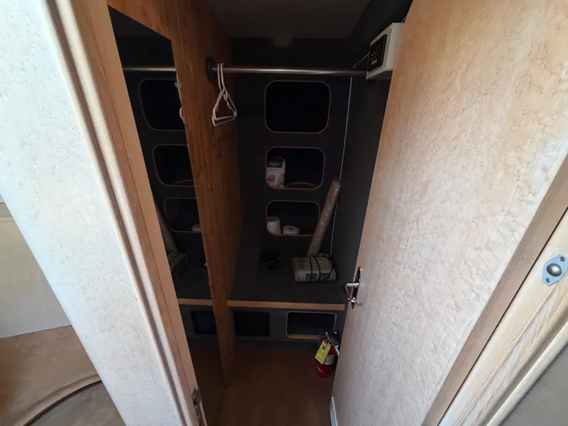 Slide: The Image of A narrow storage area with shelves, a clothes rod, and a fire extinguisher. Wooden doors and light walls. - 31