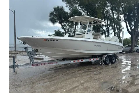 Slide: The Image of 2022 Boston Whaler 270 Dauntless boat on trailer, parked near trees and water. - 3