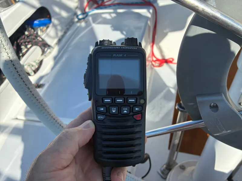 Slide: The Image of A hand holds a radio on a boat with a steering wheel and ropes in the background. - 24