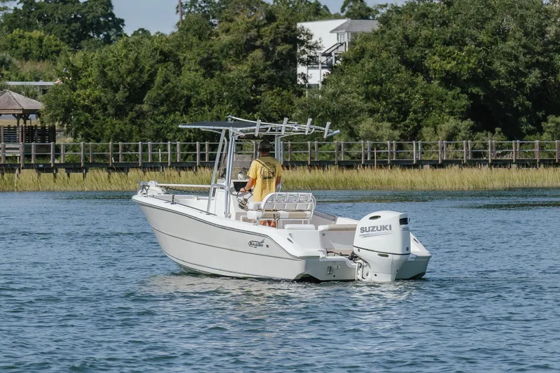 Slide: The Image of 2019 Bulls Bay 230 Center Console boat on water with Suzuki engine, near lush greenery. - 3