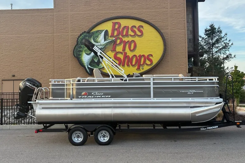 The Image of A 2025 Sun Tracker Fishin' Barge 20 DLX on a trailer in front of a Bass Pro Shops sign. - 0