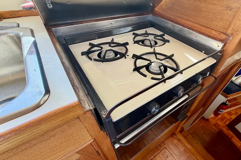 Slide: The Image of 1975 Grand Banks 32 Sedan kitchen with a three-burner stove and wooden cabinetry. - 17