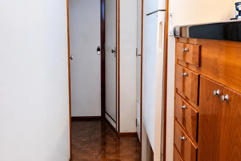 Slide: The Image of Narrow hallway inside 1981 Bertram 46.6 yacht with wooden cabinets and white walls. - 9