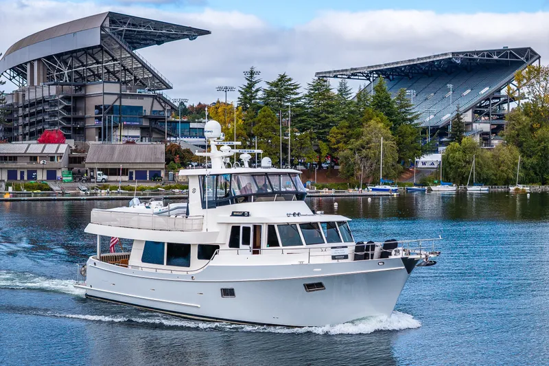 The Image of 2011 Ocean Alexander 60 Trawler cruising near a stadium with lush greenery. - 0