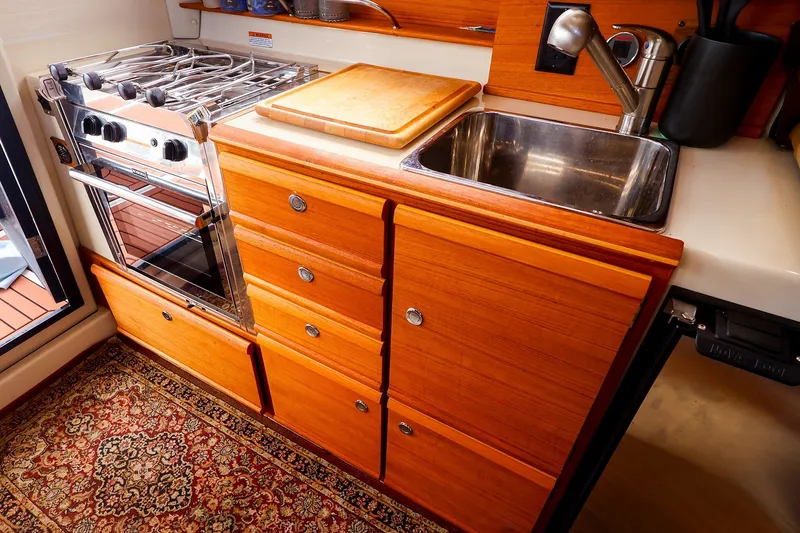 Slide: The Image of 2023 Ranger Tugs R-27 galley with stove, sink, wooden cabinetry, and decorative rug. - 20