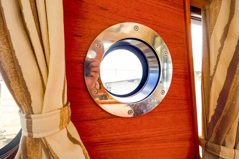Slide: The Image of Porthole view inside 2023 Ranger Tugs R-27 boat with wooden interior and curtains. - 34
