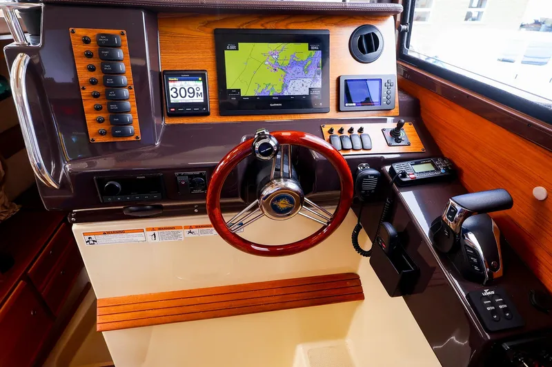 Slide: The Image of 2023 Ranger Tugs R-27 helm with navigation screens, controls, and wooden steering wheel. - 29