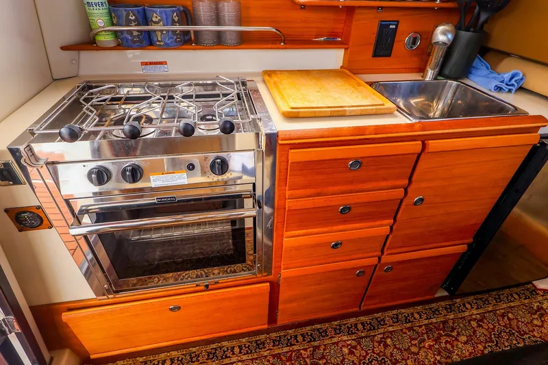 Slide: The Image of Compact kitchen in 2023 Ranger Tugs R-27 with stove, sink, and wooden cabinetry. - 21