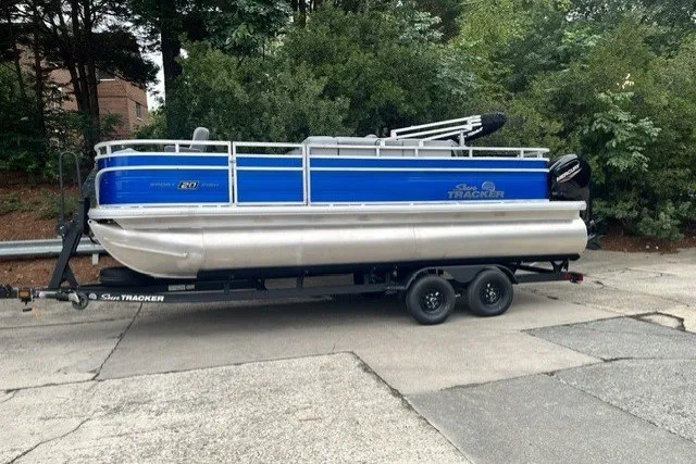 The Image of 2027 Sun Tracker SportFish 20 DLX pontoon boat on trailer, parked outdoors. - 0