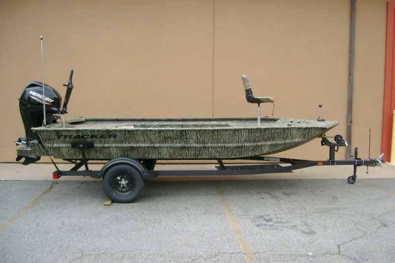 The Image of 2027 Tracker Grizzly 1654 T Sportsman boat on trailer, camo design, parked outdoors. - 0