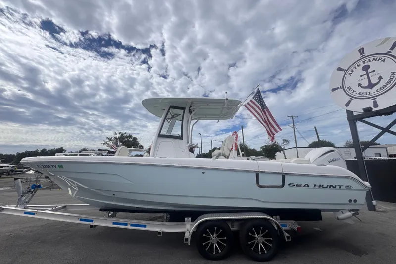 Slide: The Image of 2024 Sea Hunt Escape 25 boat on trailer, American flag, cloudy sky background. - 10