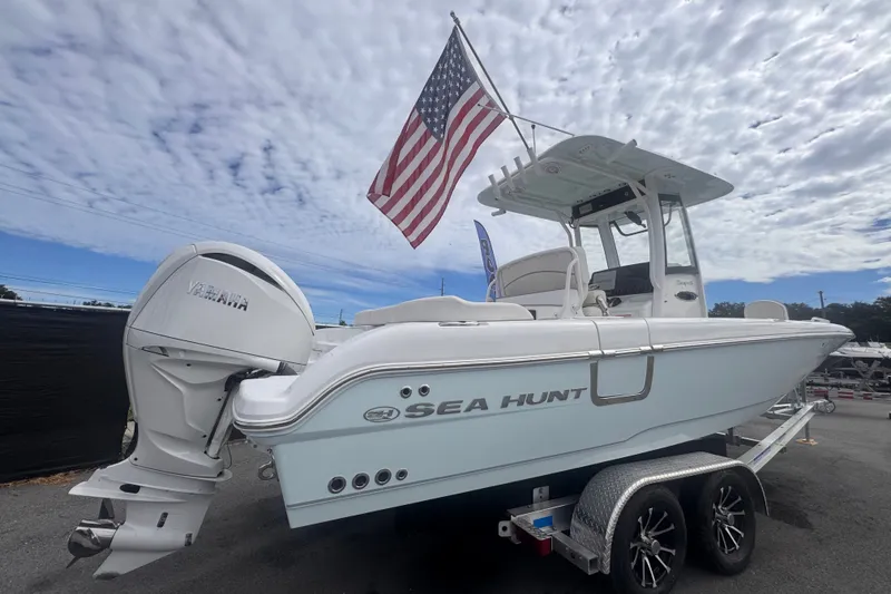 Slide: The Image of 2024 Sea Hunt Escape 25 boat with Yamaha engine and American flag, on trailer under cloudy sky. - 2