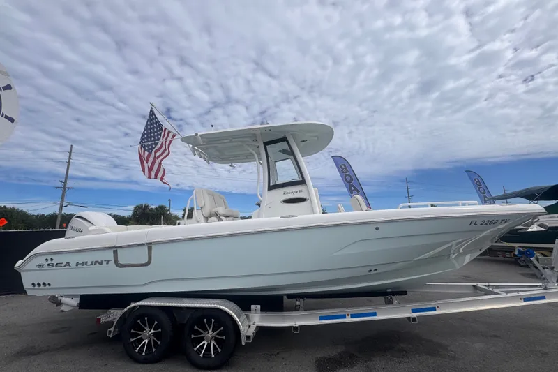 Slide: The Image of 2024 Sea Hunt Escape 25 boat on trailer with American flag, under cloudy sky. - 1
