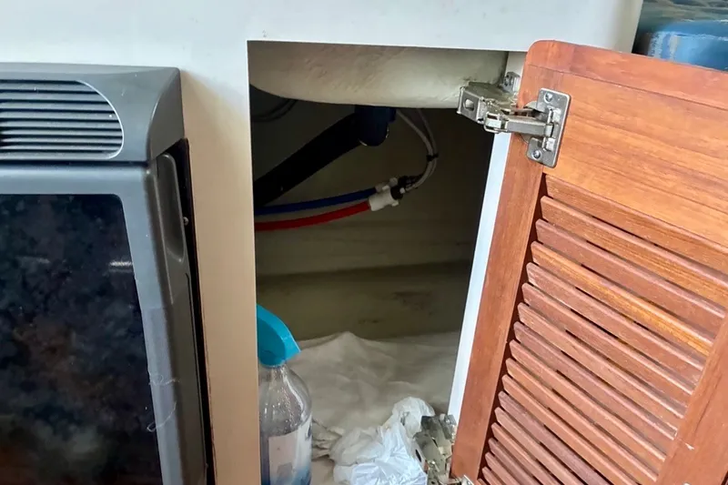 Slide: The Image of Open cabinet on a 2002 Pursuit 3000 Express boat, showing interior plumbing and cleaning supplies. - 46