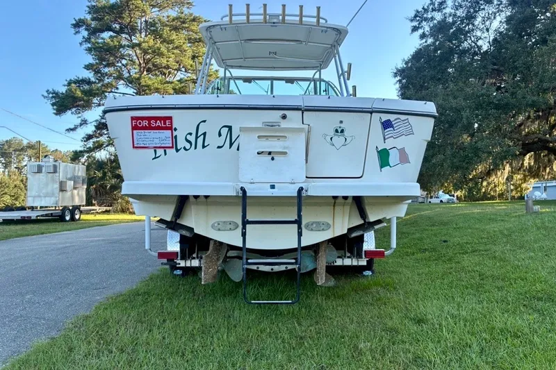 Slide: The Image of 2002 Pursuit 3000 Express boat for sale, parked on grass with flags and ladder. - 18