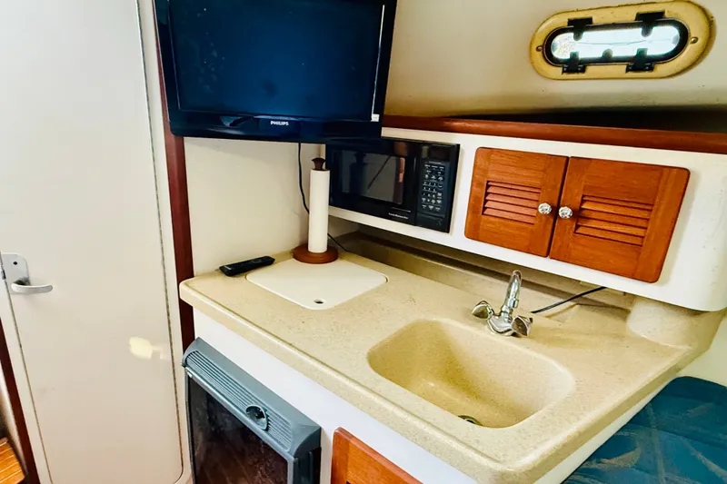 Slide: The Image of 2002 Pursuit 3000 Express boat interior with sink, TV, and wooden cabinets. - 11
