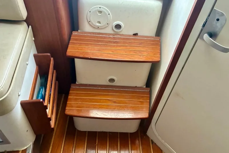 Slide: The Image of Wooden steps inside a 2002 Pursuit 3000 Express boat, featuring a compact storage area. - 42