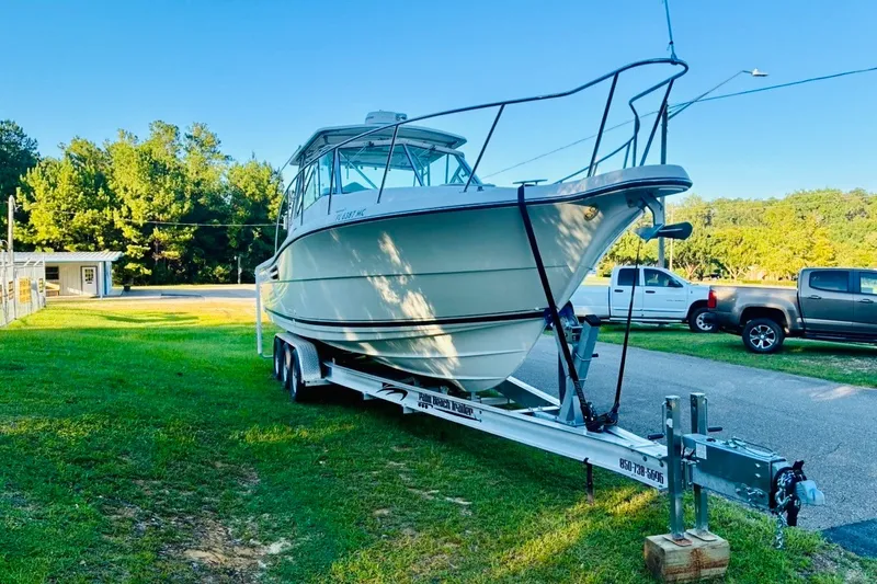 Slide: The Image of 2002 Pursuit 3000 Express boat on trailer, parked on grass with trees in background. - 89