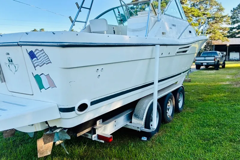 Slide: The Image of 2002 Pursuit 3000 Express boat on trailer, parked on grass with flags and decals. - 84