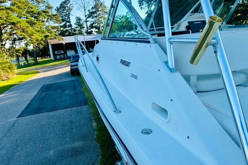Slide: The Image of 2002 Pursuit 3000 Express boat parked on a driveway near trees and a building. - 70