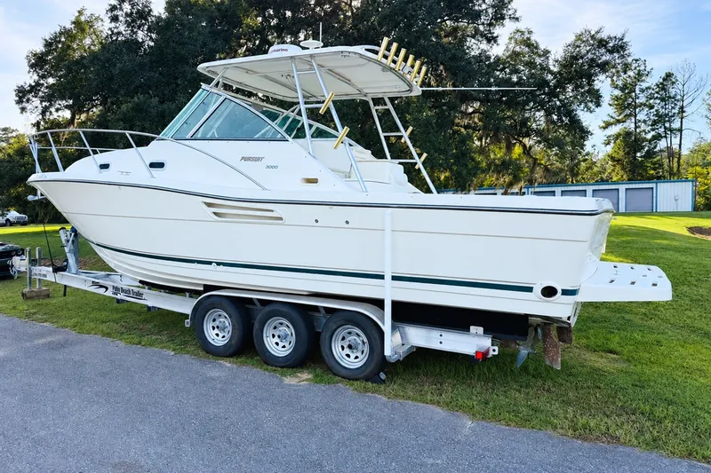 Slide: The Image of 2002 Pursuit 3000 Express boat on trailer, parked on grass with trees in background. - 3