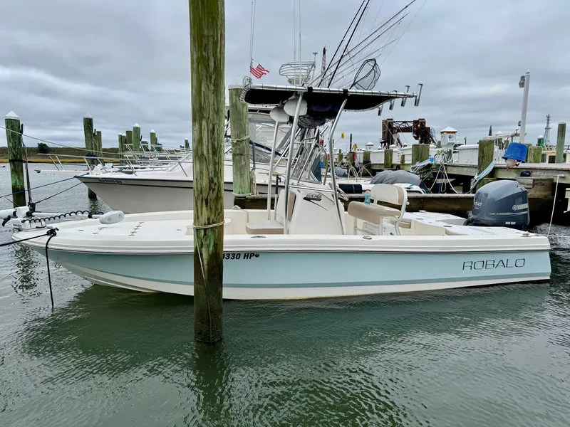 Slide: The Image of A 2015 Robalo 206 Cayman docked. It features a T-top and an outboard motor. - 0