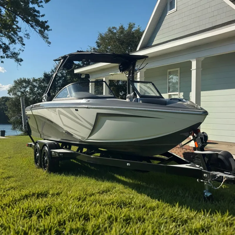 Slide: The Image of A 2018 Tigé R23 boat on a trailer, parked on grass in front of a house. - 0