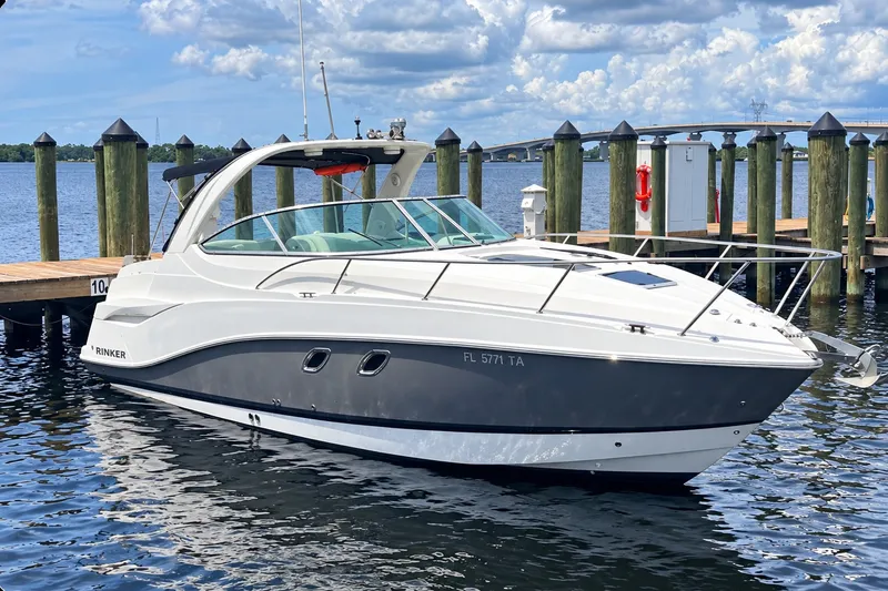 Slide: The Image of 2013 Rinker 310 Express Cruiser docked on a sunny day, with scenic water and bridge backdrop. - 2