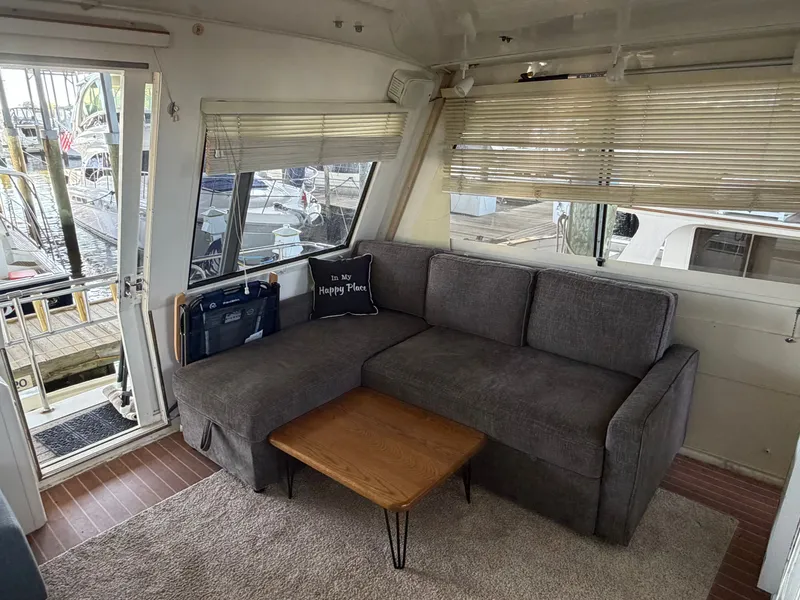 Slide: The Image of The image shows the interior of a 1991 Hatteras 52 Cockpit Motor Yacht with a gray sofa and small wooden table. - 14